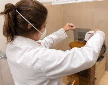 A student in a lab coat and face mask working in a lab
